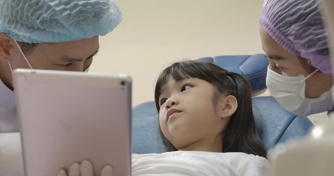 Dentist showing teeth x-ray image on digital tablet to patient. Dentist and patient choosing treatment in a consultation with medical equipment in the background.