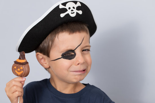 Boy in a pirate costume with sweets in hand on gray background