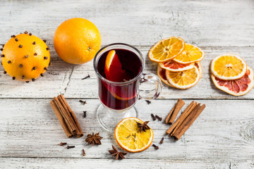 Glass of delicious mulled wine with oranges anise cinnamon on white wooden table