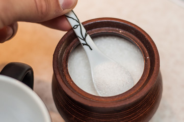 Picking sugar from a sugar bowl with a small ceramic spoon.