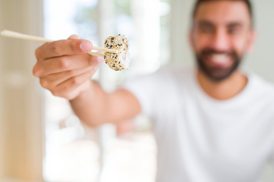 Handsome man smiling happy enjoying eating fresh colorful asian sushi using chopsticks