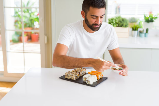 Handsome man smiling happy enjoying eating fresh colorful asian sushi using chopsticks