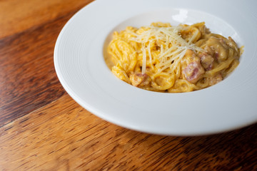 Delicious spaghetti, bacon topped with cheese, served on a white plate on brown wooden table top