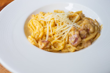 Delicious spaghetti, bacon topped with cheese, served on a white plate