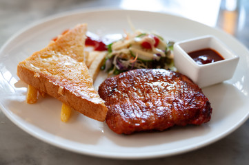 Appetizing steak with toasted fries, vegetables, tomato sauce, served on a white plate
