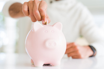 Obraz na płótnie Canvas Man putting a coin inside of piggy bank saving for investment