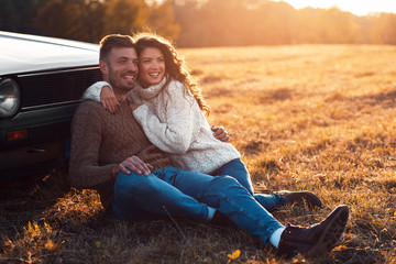 Beautiful young couple enjoying time together outdoor sitting on meadow leaning on old fashioned...