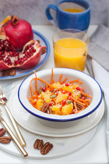 Healthy raw vegetarian salad with carrot, pomegranate seeds, oranges, pumpkin seeds, pecan nuts. Glass of orange juice and pomegranate on the background.