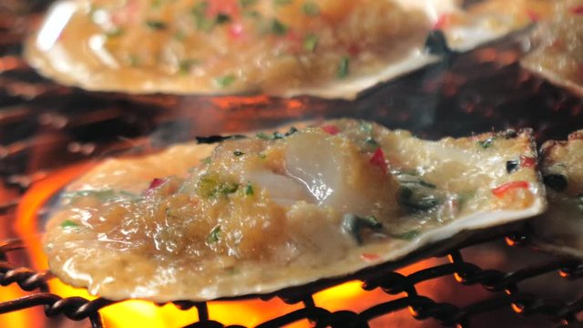 Big fresh scallop shell seafood grill on metal net with charcoal, barbecue in korean restaurant. Barbecue cooking style