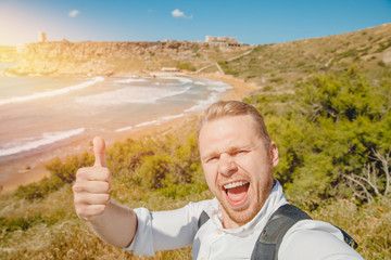 Male traveler makes selfie photo on background of blue sea, sand beach with backpack. Travel concept