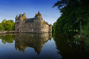 Fototapeta na wymiar the historic Chateau Trecesson castle reflected in the pond in cool dark blue evening light