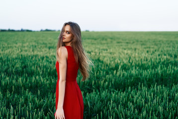 Beautiful young woman in red dress posing outdoors in green summer field
