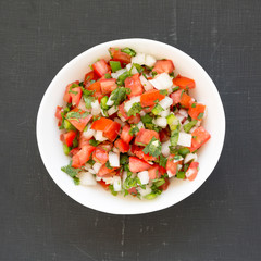 Pico de Gallo in a white bowl on a black surface, overhead view. Top view, from above, flat lay. Close-up.