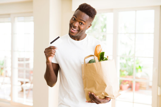 African american man holding paper bag full of groceries and holding credit card as payment