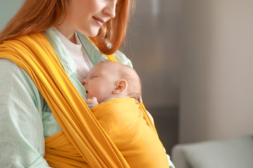 Young mother with little baby in sling at home