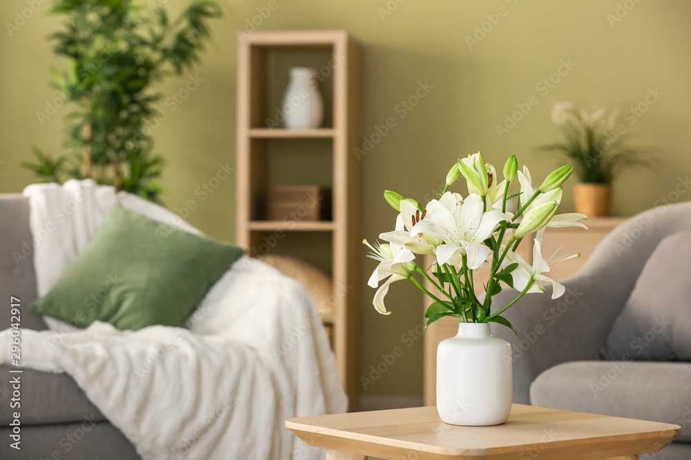 Wall mural beautiful lily flowers in vase on table in room