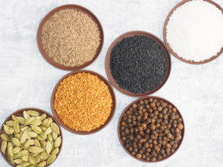 Spices and herbs set on concrete background in clay plate. Cumin (jeera), black cumin, fenugreek, allspice, green cardamom, coconut flake. Modern apothecary, naturopathy and ayurveda concept.