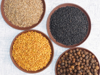Spices and herbs set on concrete background in clay plate. Cumin (jeera), black cumin, fenugreek, allspice. Modern apothecary, naturopathy and ayurveda concept.