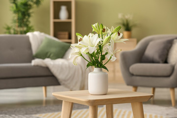 Beautiful lily flowers in vase on table in room