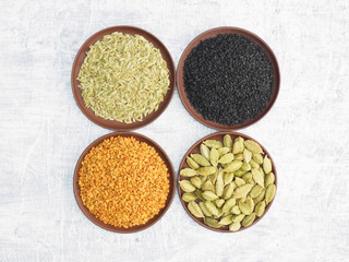 Spices and herbs set on concrete background in clay plate. Black cumin, fenugreek, fennel, green cardamom. Modern apothecary, naturopathy and ayurveda concept.