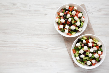 Homemade Shepards salad with cucumbers, feta and parsley in white bowls on a white wooden background, top view. From above, overhead, flat lay. Copy space.