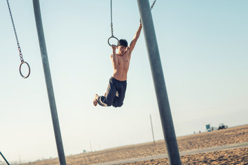 A young man athlete working out on traveling rings on muscle beach, Santa Monica, California