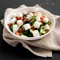 Homemade Shepherds salad with cucumbers, parsley and feta in a white bowl on a black table, low angle view. Close-up.