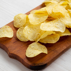 Yellow potato chips with salt on a rustic wooden board, side view. Close-up.