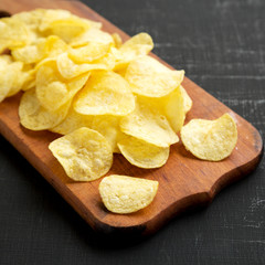 Crispy potato chips with salt on a rustic wooden board on a black background, side view. Close-up.