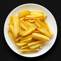 Homemade french fries on a white plate on a black surface, top view. Flat lay, overhead, from above. Closeup.