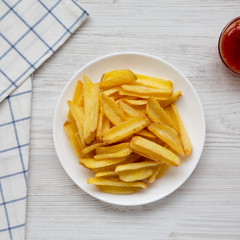 Homemade french fries with sour-sweet sauce on a white plate on a white wooden table, top view. Flat lay, overhead, from above. Close-up.