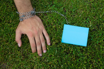 A hand tied to a color sticker with a metal chain, on a background of grass lawn, toned, with copy...
