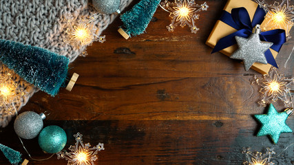 Wrapping rustic blue theme Christmas holiday gifts with kraft brown paper on vintage dark wood table, nightime overhead flat lay with copy space.
