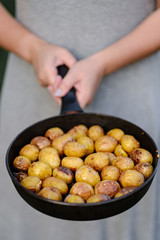 girl holds pan with whole baked potatoes.