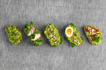 Variety of open bruschetta sandwiches with avocado, soft boiled egg, radish, spinach, herbs and nuts on a grey background. Healthy food. Healthy breakfast