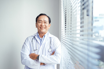 Thoughtful male doctor standing arms crossed in hospital
