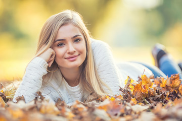 Autumn portrait of young woman lying on maple leaves in park