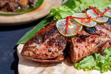 Fried fish with fresh green salad and lemon of Bali, Indonesia, closeup. Delicious roasted sea fish with lemon on wooden plate in restaurant