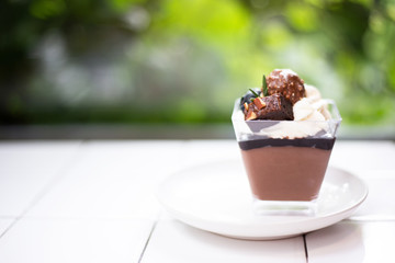 Closeup dark chocolate mousse in glass put on white desk with blur nature background. 