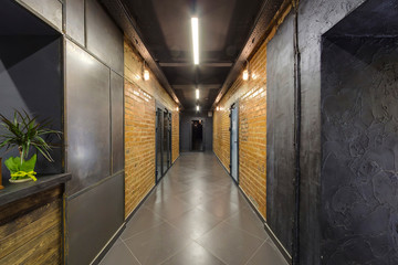 Long dark corridor and doors. Brick walls. Ceramic tiles on the floor. Modern interior