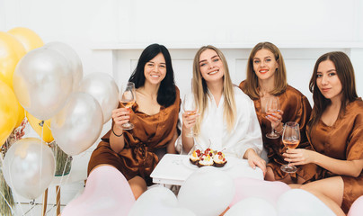 hen party. Beautiful charming women wearing in satin robe drinking alcohol and enjoying pajamas...