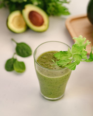 Green smoothie with a stalk of celery in a glass cup. On the table is an avocado.
