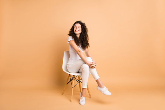 Full length photo of amazing lady looking interested empty space sitting comfy chair good mood inspired wear casual clothes isolated beige pastel color background