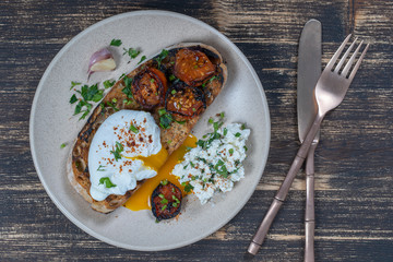 Poached egg on a piece of bread with fried red tomato, garlic and cottage cheese on a plate, close up