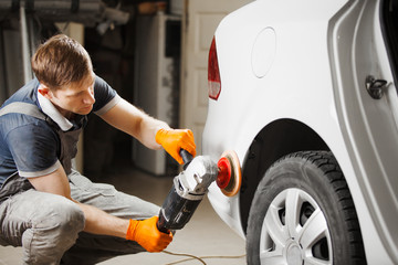 Worker cleaning white car with polishing and waxing, close-up. Auto repair shop.