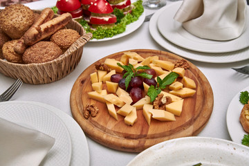 Small pieces of cheese of different varieties lie on a wooden plate on a served table in restaurant.