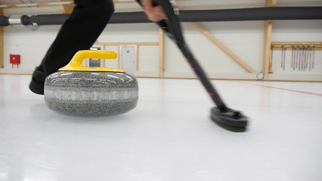 Curling game. Curler is sweeping the ice surface in the path of the stone. Curling granit stone is sliding and broom or brush is sweeping. Concept: winter games, winter olympic sports.