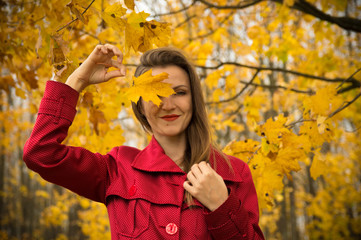 Warm autumn. Beautiful girl in a red coat holds yellow leaves in the autumn park.