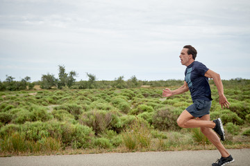 runner doing a sprint with speed face, from right to left, runs along a paved road