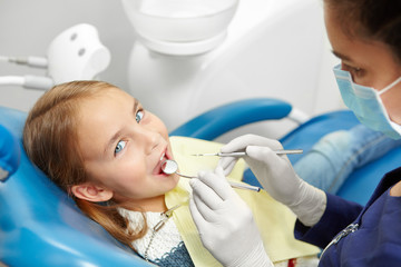 Female dentist examining little girl teeth in pediatric dentistry clinic.